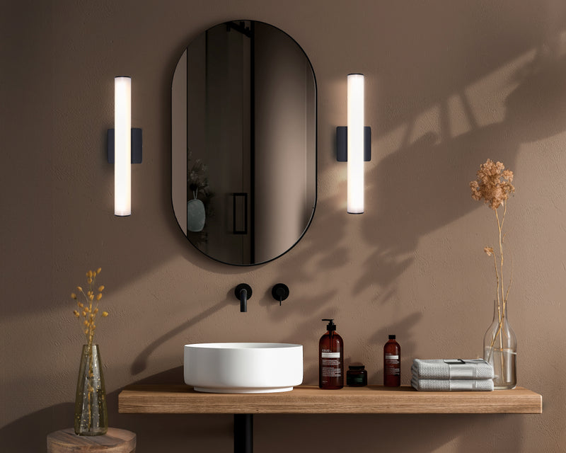 Matte black LED tube vanity sconces mounted beside oval bathroom mirror above vessel sink on floating wood shelf